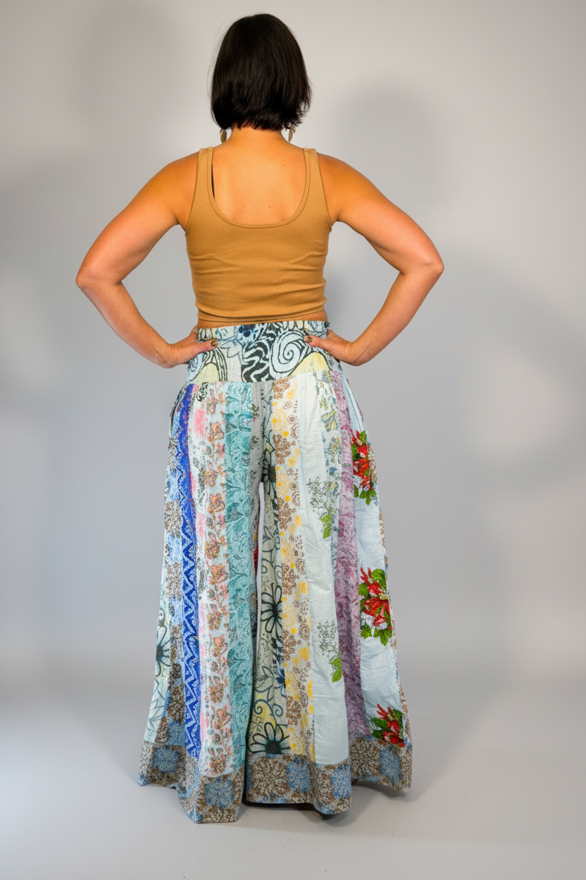 Model wearing the Savvy Munk Meadows of Nepal Palazzo Pants with colorful floral patchwork patterns, styled with a tan crop top against a clean studio background