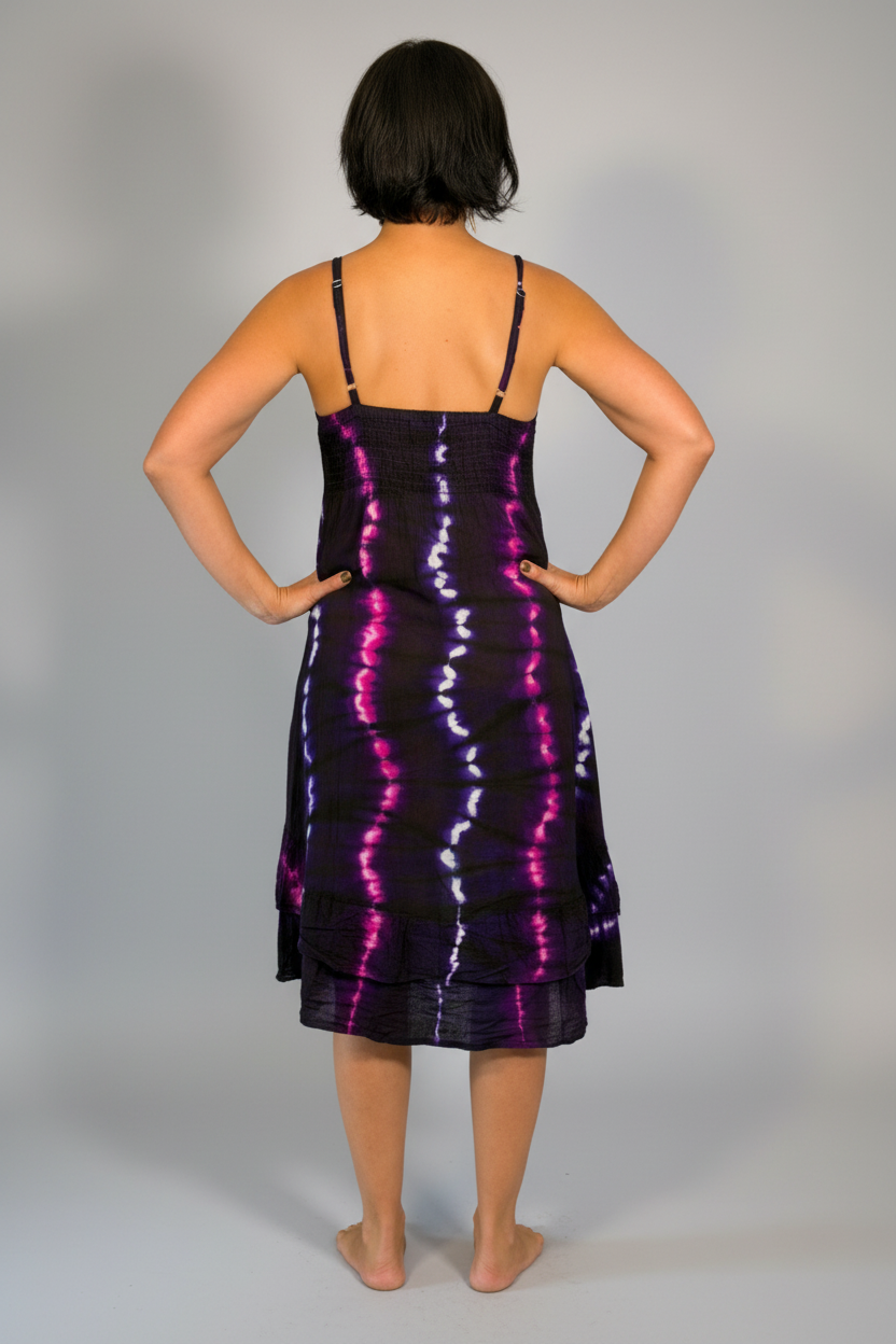 Model modeling the Savvy Munk Electric Orchid Tiered Maxi Dress, a sleeveless V-neck dress with a striking black, blue, and hot pink tie-dye pattern. She is standing barefoot on a neutral-toned wood floor against a plain light gray wall in a studio setting.