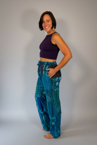 Model wearing Savvy Munk Mystic Moon Teal Celestial Patchwork Pants paired with a dark purple crop top against a neutral studio backdrop