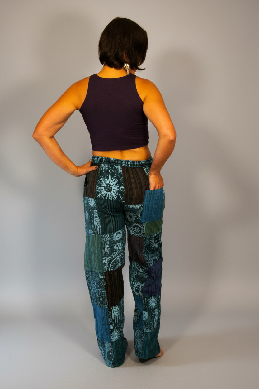 Model wearing Savvy Munk Mystic Moon Teal Celestial Patchwork Pants paired with a dark purple crop top against a neutral studio backdrop