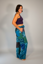 Model wearing Savvy Munk Mystic Moon Teal Celestial Patchwork Pants paired with a dark purple crop top against a neutral studio backdrop