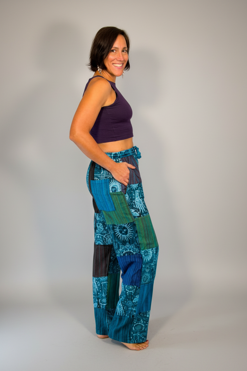 Model wearing Savvy Munk Mystic Moon Teal Celestial Patchwork Pants paired with a dark purple crop top against a neutral studio backdrop