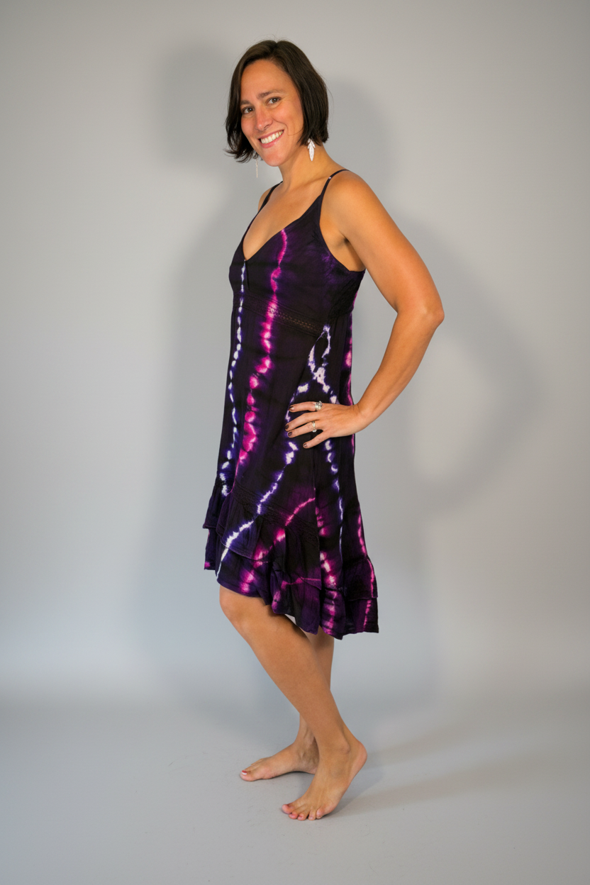 Model modeling the Savvy Munk Electric Orchid Tiered Maxi Dress, a sleeveless V-neck dress with a striking black, blue, and hot pink tie-dye pattern. She is standing barefoot on a neutral-toned wood floor against a plain light gray wall in a studio setting