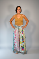 Model wearing the Savvy Munk Meadows of Nepal Palazzo Pants with colorful floral patchwork patterns, styled with a tan crop top against a clean studio background