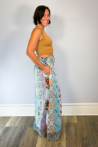 Model wearing the Savvy Munk Meadows of Nepal Palazzo Pants with colorful floral patchwork patterns, styled with a tan crop top against a clean studio background.