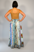 Model wearing the Savvy Munk Meadows of Nepal Palazzo Pants with colorful floral patchwork patterns, styled with a tan crop top against a clean studio background