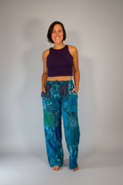 Model wearing Savvy Munk Mystic Moon Teal Celestial Patchwork Pants paired with a dark purple crop top against a neutral studio backdrop